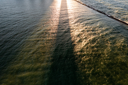 A beautiful aerial drone view of a thick dark shadow on the green water of Lake Michigan from a high-rise building with bright yellow sunlight reflecting off the surface at sunset.