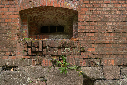 Old red brick wall with a small window on an autumn day.