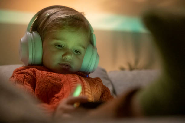 Kid uses phone and headphones to watch TV. Happy childhood. Family time at home. screen time and technology in babies stock pictures, royalty-free photos & images