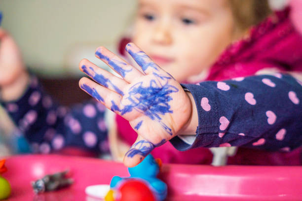 Girl draws with felt tip pens over herself while sitting on baby pot.