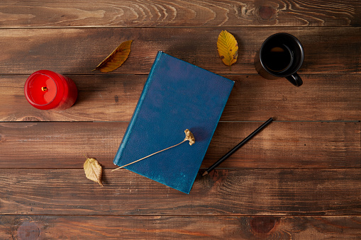 Pencil and book wooden background with cup of coffee, candle and autumn leaves.