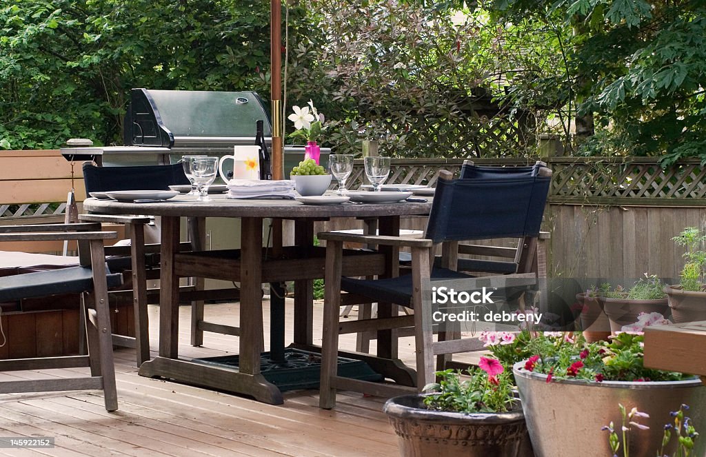 Wooden outdoor table and chairs on a patio with a barbeque lunch on the patio - the table is set Dining Stock Photo