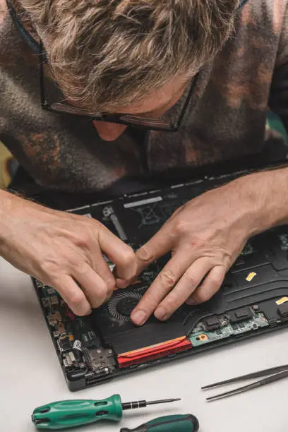 Photo of computer repairman removes the laptop cooling system from the case for cleaning and maintenance.