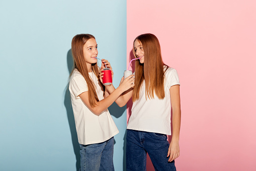 Party. Happy girls, two sisters friends in casual style clothes isolated over pink-blue studio background. Concept of modern youth fashion, relationship, emotions, beauty and youth.