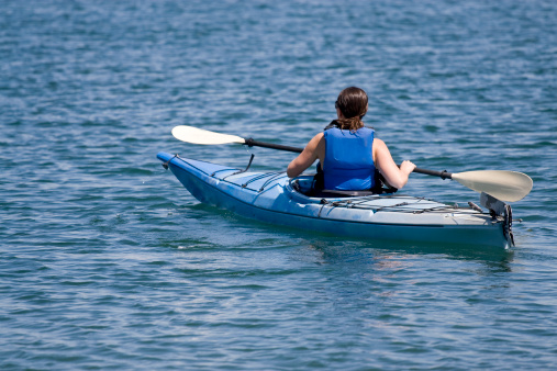 A woman in an ocean kayak on calm blue water.
