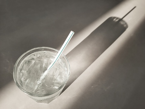 Glass of drinking water with ice cubes and shadow - white table background.