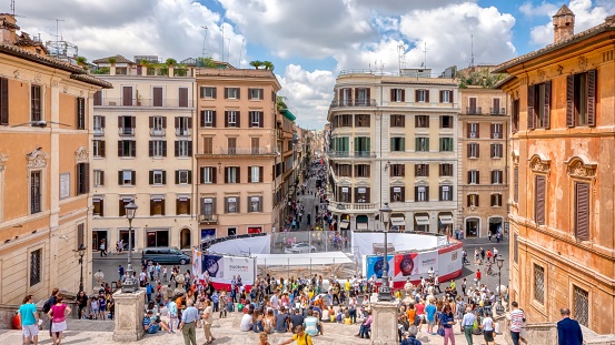 Rome, Italy - June 18, 2014: Tourists gathered near the closed Fontana della Barcaccia, fenced off for restoration work, at the bottom of the Spanish Steps. Beautiful building facades surround the area.