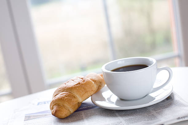 Cup of coffee with a croissant and a newspaper stock photo