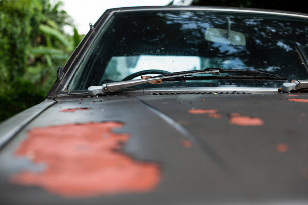 Close-up a grey old car bonnet with crack and scratch color skin. A vintage sedan Japanese car left unattended on street with ripped off and peeled skin cracked pattern found all over. Selective focus.