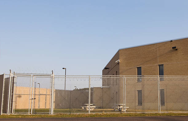 An empty fenced prison yard with prison behind stock photo