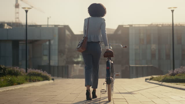 Bicycle, travel and black woman walking in city street for budget, saving and carbon footprint, eco friendly transport. Rear of a gen z person, employee or worker and cycling bike on an urban road