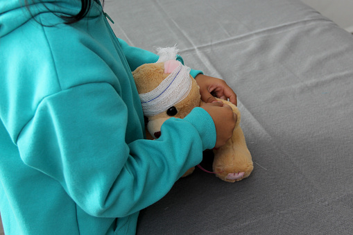 4-year-old brunette Latina girl with glasses represents mistreatment and physical abuse in her teddy bear with bandages on her head