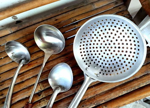 Cooking utensils (ladle and colander) on bamboo table.