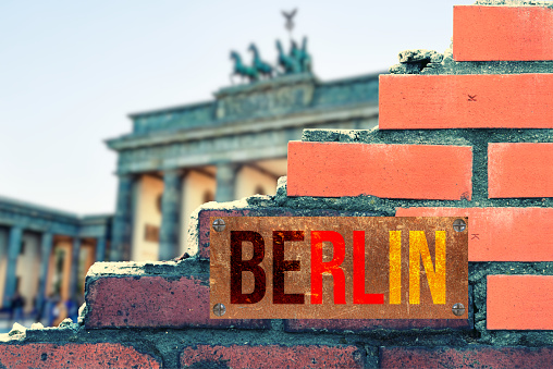 Eine Mauer, ein Blick auf Brandenburger Tor und ein Schild Berlin