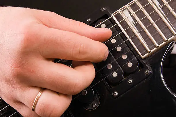 The man plays a close up of a hand on an electroguitar
