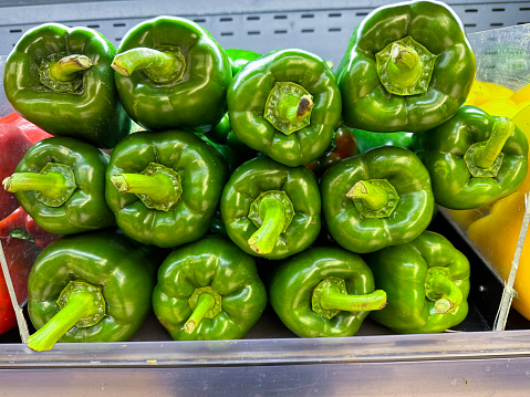 Stock photo showing a close-up view of a pile of red, green and yellow bell peppers (Capsicum) being sold from a produce display at the fruit and vegetable grocery section of a supermarket.