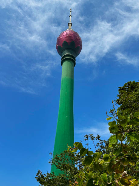 Stock photo showing close-up view from below of the symbolic landmark Lotus Tower, Colombo, Sri Lanka. The lotus symbolises purity within Sri Lankan culture. imagen en primer plano del tallo verde y la torre de observación en forma de pétalos de flores rosadas de la torre del loto de colombo, sri lanka, punto de referencia turístico de la torre de comunicaciones, fondo de cielo nublado, visto desde abajo