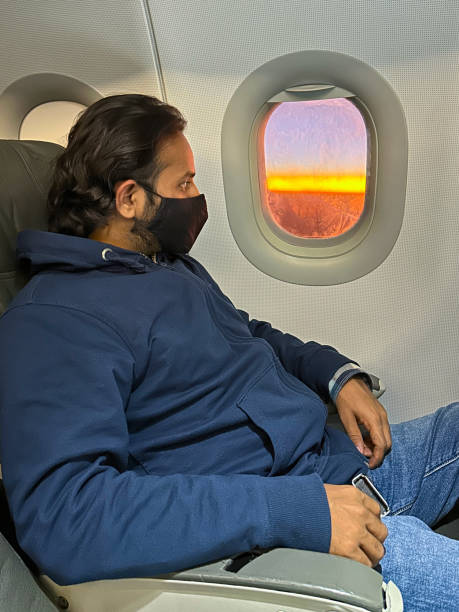 Stock photo taken at dusk as the sun sets showing the wing of a plane pictured through the airplane window. The focal point of this picture is the dramatic orange sunset. imagen en primer plano de un hombre indio en el asiento del avión con una máscara facial médica para protección, virus coronavirus covid-19, contaminación, gripe aviar, problema respiratorio, neumonía viral, sars, enfermedades, cuarentena y enfermeda