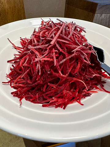 Stock photo showing close-up, elevated view of grated beetroot piled high in a white bowl with metal serving tongs. Raw beetroot is considered to be a very healthy snack food and boasts a list of health benefits including possible aid to weight loss.