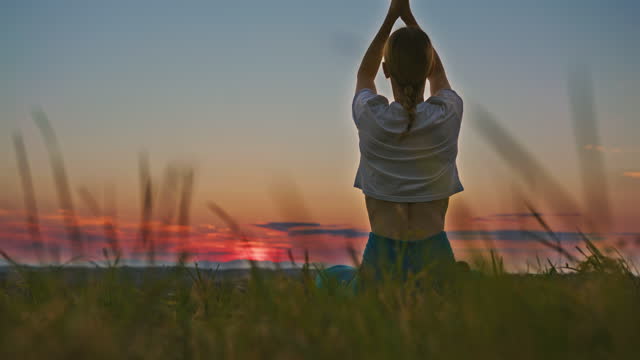 Woman with blond hair practicing yoga on a hill in Jeruzalem,sun behind her