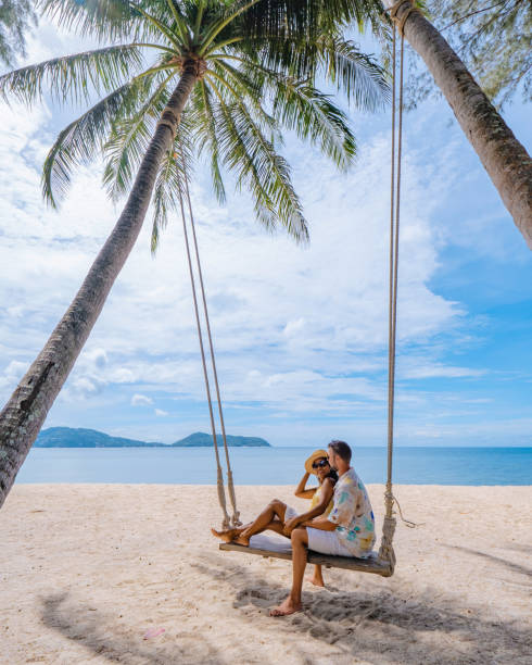 couple on the beach in phuket relaxing on beach swing chair, tropical beach in Phuket Thailand couple on the beach in Phuket relaxing on a beach swing chair, tropical beach in Phuket Thailand. Nakalay beach thailand beach stock pictures, royalty-free photos & images