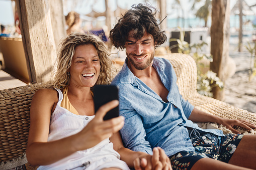Young happy couple reading a text message on smart phone during summer day on the beach.