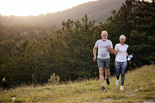 Happy mature couple running during sports training in nature. Copy space.
