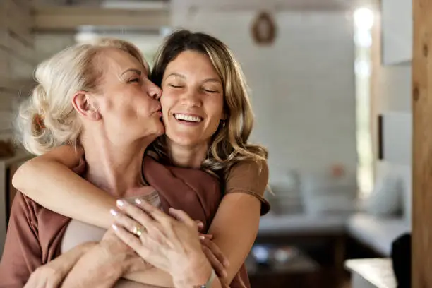 Loving mature single mother kissing her adult daughter at home.