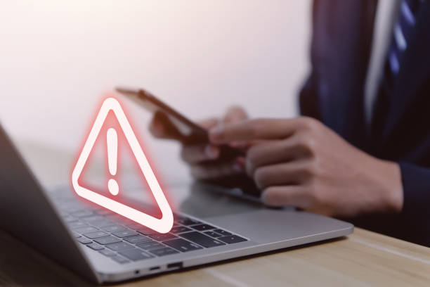 istock Businessman using laptop showing warning triangle and exclamation mark A warning about a dangerous problem is showing up on your computer. 1459278658
