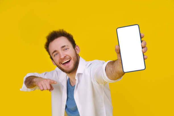 istock Great offer. Young happy man holding smartphone showing a white empty screen and exciting to win isolated over yellow background, celebrating success. Product placement. Empty space or copy space 1459280255