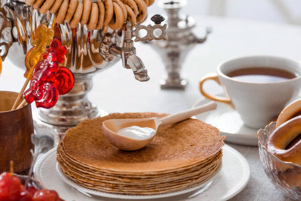 istock Russian traditions. Russian holiday Maslenitsa. Still life with a cup of tea, a stack of pancakes, sour cream, honey, cubes of butter, bagels, dried fruits, caramel cockerel and samovars. 1459282916