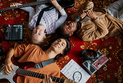 Top view shot of smiling music band lying on ornate carpet in studio and looking at camera