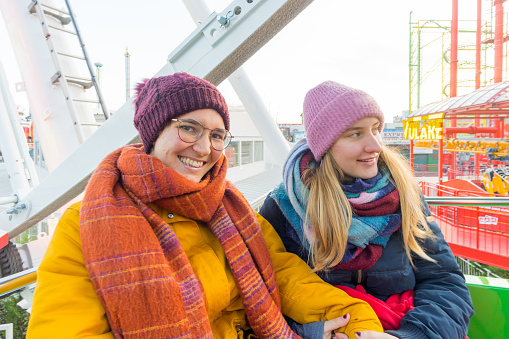 A close-up shot of a happy Caucasian lesbian couple in winterwear sitting on the Ferris wheel