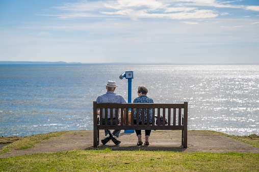 Aberystwyth, United Kingdom – May 18, 2022: Elderly couple staring out at the ocean sitting on the bench on the shore