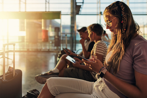 Adolescentes esperando en el aeropuerto y jugando con dispositivos inteligentes photo