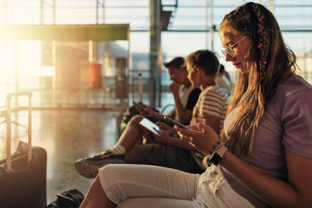 adolescentes esperando en el aeropuerto y jugando con dispositivos inteligentes - airport waiting room waiting airport lounge fotografías e imágenes de stock