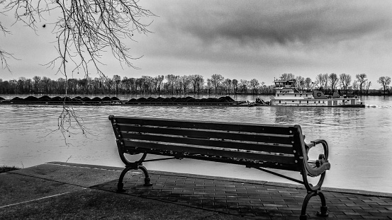 A grayscale shot of a wooden bench on the shore of Ohio river in Newburgh