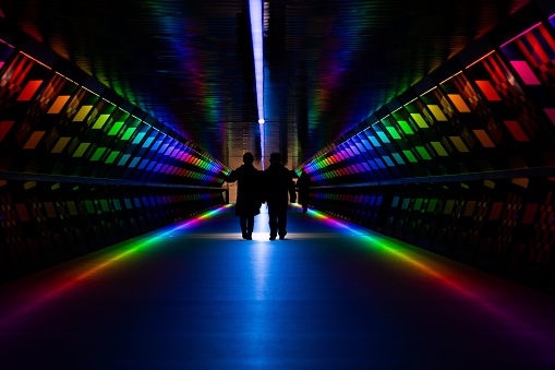 A colorful pedestrian tunnel with bright neon lights and silhouettes of people walking through it