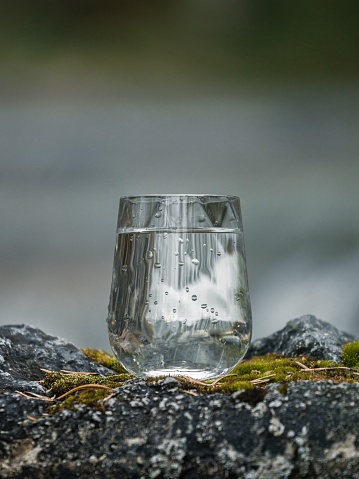 A closeup shot of a glass cup of water on a rocky surface reflecting a rounf with blurred background
