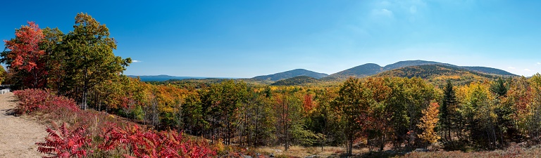 A panoramic view of New England's fall foliage with mountains and a bright sky in the background