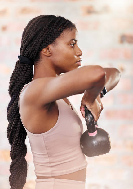 fitness, allenamento e donna nera in palestra con kettlebell per la forza muscolare e la vista laterale dell'allenamento. benessere, esercizio fisico e concentrazione di una ragazza sana che solleva pesi con concentrazione per la resistenza del corpo. - endurance sport foto e immagini stock