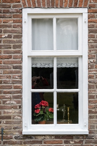 A vertical shot of white window in an old house with flowers in the background