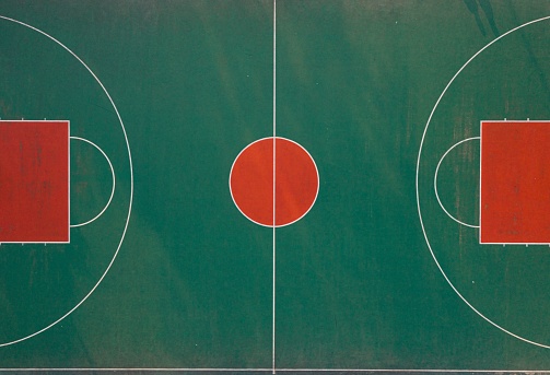 An aerial top view of an empty basketball court in green and red colors
