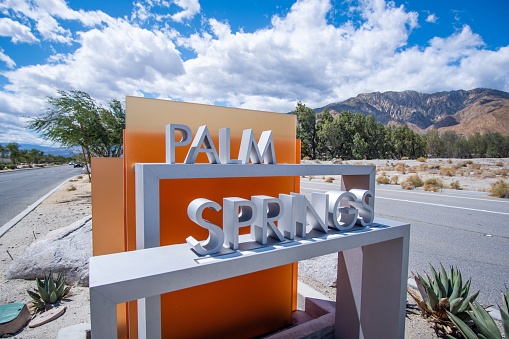 The Palm Springs sign in California, USA against mountain landscape and cloudy day