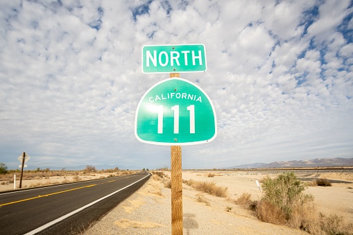 A closeup shot of a North California 111 sign on the side of a road under cotton-like clouds