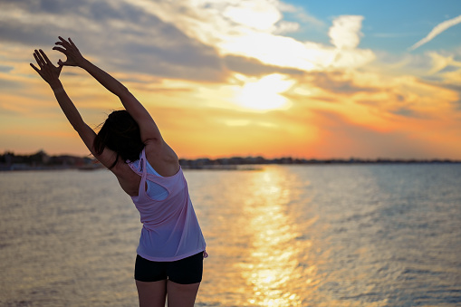 Woman practices yoga and meditates with the sunset view on the sea.