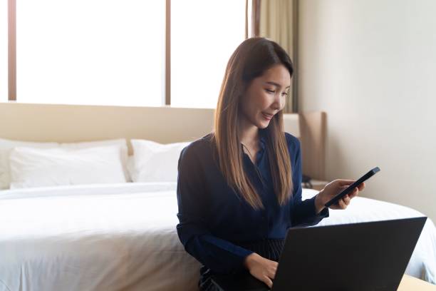istock Happy Thai woman checking her phone while using a laptop in the hotel room 1459304725