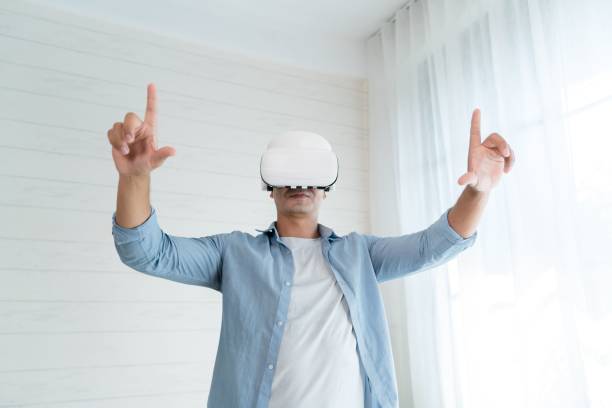 istock Happy man in a VR headset with open hands enjoying a virtual reality experience in a white bedroom 1459304812