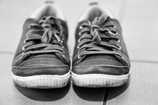 A grayscale closeup of sneakers on the floor. Selected focus.