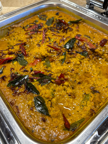 Stock photo showing close-up view of Dal tadka curry meal recipe in a stainless steel hot plate warmer dish at a restaurant self service dinner buffet. Toor dal (split pigeon peas), moong dal (split yellow lentils) and masoor dal (split red lentils) cooked with butter, herbs and spices.
